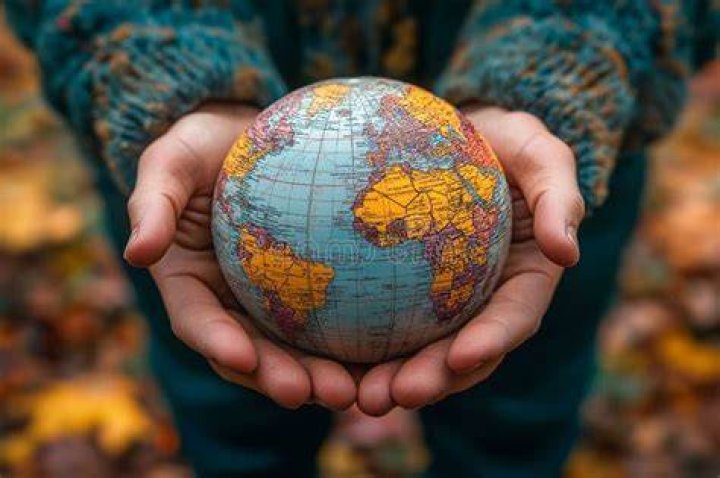person holding globe at elbow standing on grass