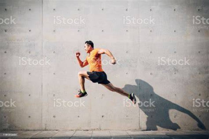 sporty asian mid man running and jumping against shutter health and fitness concept