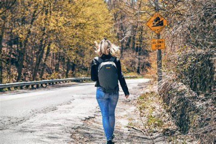 Woman walks along a windy rural road wearing a backpack
