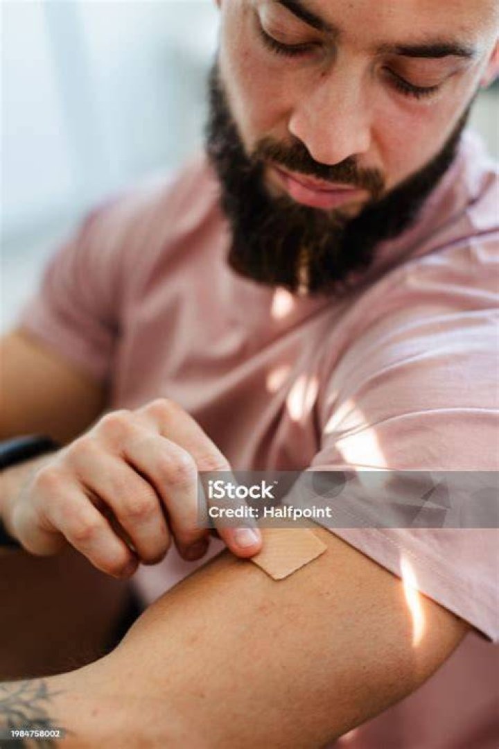 Young man putting nicotine patch on arm, upper half young man putting nicotine patch on arm, upper half